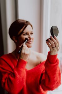 Kaboompics - A woman in a red sweater does her make-up - applies a foundation with a brush