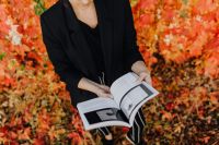 Kaboompics - Woman in a Black Blazer Holding an Open Design Book amid Colorful Fall Leaves