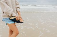 Kaboompics - Close-Up of a Woman Holding a Closed Book Beside the Sea in Denim Shorts