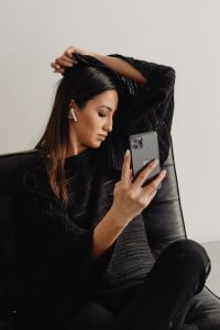 Kaboompics - Woman Checking a Smartphone in a Leather Chair with Earbuds