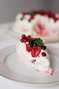 Kaboompics - Pavlova Slice in Focus with a Berry-Topped Cake Softly Blurred Behind