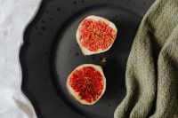 Kaboompics - Two Fresh Fig Halves on Black Stoneware with Olive Green Knit, Seasonal Recipe Still Life