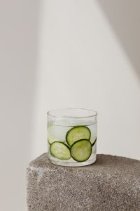 Kaboompics - Minimal Cucumber-Infused Water Glass on a Rough Stone Pedestal, Front-Facing Vertical Drink Background with Copy Space