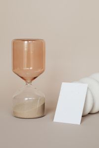 Kaboompics - Vertical Blank Business Card Leaning Beside an Amber Hourglass and White Ceramic Forms, Neutral Mockup