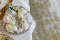 Kaboompics - Glass Easter Egg Ornaments with White Feathers and Green Ribbon in a Decorative Bowl