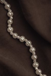 Kaboompics - Pearl Bead Strand on Dark Brown Fabric with Copy Space