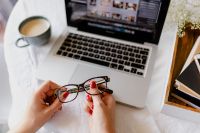 Kaboompics - Woman Holding Eyeglasses beside Laptop and Coffee During a Photo Editing Break at Home