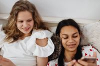 Kaboompics - Close-Up of Two Teen Girls Looking at a Phone While Relaxing on a Bed