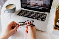 Kaboompics - Laptop Photo Editing Workspace with Coffee and Eyeglasses Held in Hands on White Bedding