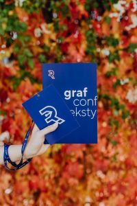 Kaboompics - Vertical Close-Up of a Blue Grafconf Book and Conference Pass in Hand, Autumn Foliage