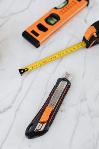 Kaboompics - Vertical Close-Up of an Orange Level, Tape Measure and Utility Knife on White Marble