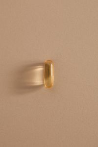 Kaboompics - Single Golden Softgel Capsule on a Beige Background