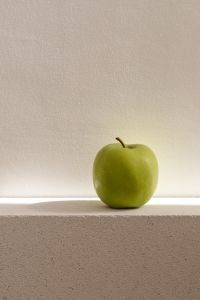 Kaboompics - Centered Green Apple on a Stone Ledge Beneath a Sunlit Textured Wall, Minimal Vertical Still Life