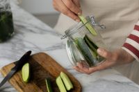 Kaboompics - Hands Filling a Clamp Jar with Cucumber Spears beside Cutting Board