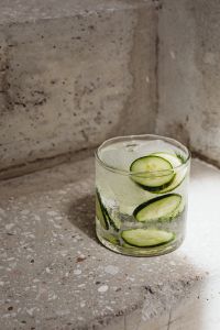 Kaboompics - Close-Up Cucumber Detox Water with Ice on Textured Concrete Steps, Sunlit Summer Drink Photography