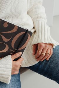 Kaboompics - Faceless Woman in White Sweater Holding Patterned Book and Gold Rings