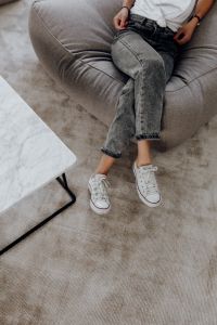 Kaboompics - Woman in Gray Jeans and White Trainers Seated on a Gray Sofa, Casual Outfit Inspiration