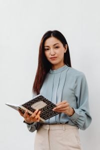 Kaboompics - Asian Woman Holding an Open Notebook Against a White Background