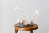 Kaboompics - Wire Chicken-Shaped Egg Basket with Glass Egg Cups on Wooden Stool, Easter Table Styling