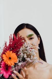 Kaboompics - Woman Peeking Through Orange Gerbera and Wildflower Bouquet, Floral Beauty Portrait