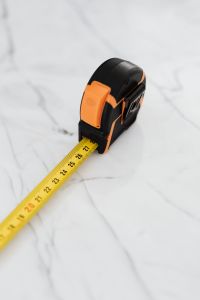 Kaboompics - Vertical Yellow Tape Measure Extended from Its Black and Orange Case on White Marble