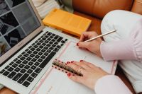 Kaboompics - Faceless Woman Writing in a Planner Beside Laptop