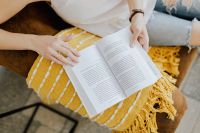 Kaboompics - The woman is reading a book. She is sitting on a brown couch and a yellow blanket