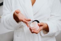 Kaboompics - Close-Up of a Woman Taking Hand Cream from an Open Jar in a White Bathrobe