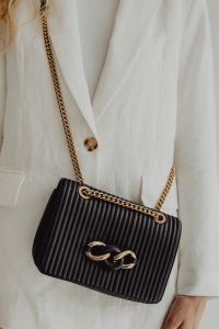 Kaboompics - Black Ribbed Chain Strap Handbag against a White Blazer, Front View