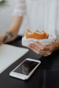 Kaboompics - Close-Up of Woman Holding Burger Beside Smartphone