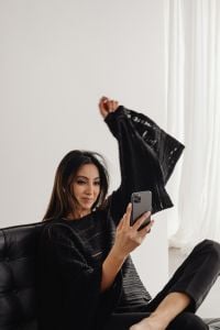 Kaboompics - Woman in a Black Knit Top Holding a Smartphone in a Leather Chair