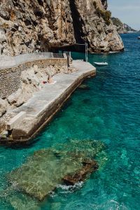 Kaboompics - Rocky Amalfi Coast Swimming Platform with Boat and Cliffside Walkway