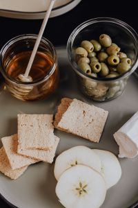 Kaboompics - Crispbread, Green Olives, Apple Slices and Honey in a Vertical Healthy Snack Flat Lay