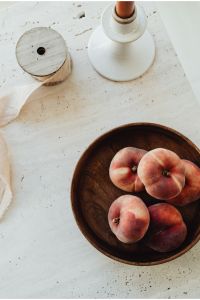 Kaboompics - Peaches in Wooden Bowl with White Candle and Neutral Copy Space