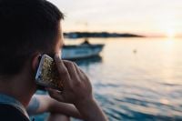 Kaboompics - Gold-Patterned Smartphone Held to a Man’s Ear Beside a Boat at Sunset