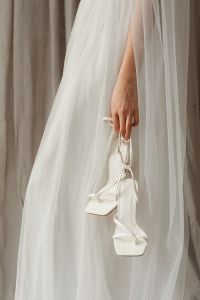 Kaboompics - Bride Holding White Strappy Wedding Heels Against Tulle