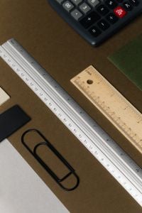 Kaboompics - Office Desk Flat Lay with Calculator, Measuring Rulers, Black Paper Clips and Papers on Brown Surface