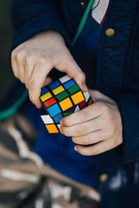 Kaboompics - Turning a Rubik's Cube in a Blue Quilted Jacket, Vertical Hands-On Puzzle Photo