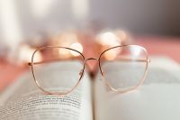 Kaboompics - Eyeglasses Resting on an Open Book in Soft Pink Light