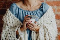 Kaboompics - A woman in a warm blanket holds a cup of coffee or tea