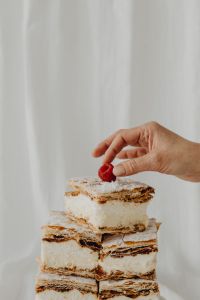 Kaboompics - Hand Garnishing a Stack of Napoleonka Cake Squares with a Raspberry