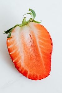 Kaboompics - Single Strawberry Half with Green Calyx on White, Fresh Fruit Ingredient Photo with Copy Space