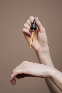 Kaboompics - Fingertips Holding a Golden Oil Dropper Against Neutral Taupe, Clean Beauty Copy Space