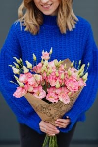Close up of woman holding bouquet of pink lisianthus flowers wrapped in brown paper