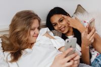 Kaboompics - Teen Friends Comparing Smartphone Screens While Relaxing on a Bed