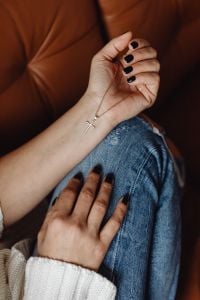 Kaboompics - Gold Cross Necklace on a Hand Resting over Blue Jeans