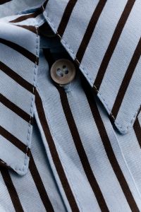 Kaboompics - Light Blue and Brown Striped Cotton Shirt Collar with Beige Button, Close-Up Fashion Fabric Detail