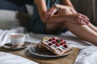 Kaboompics - Woman Seated on Bed Beside Coffee and Raspberry Waffles, Cozy Morning Lifestyle
