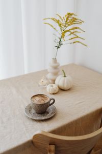 Kaboompics - Vertical Autumn Coffee Still Life with Goldenrod, Candle, White Pumpkins and Speckled Cup