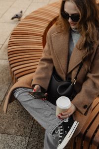 Kaboompics - Woman Using Smartphone with Coffee on a Curved Wooden Bench